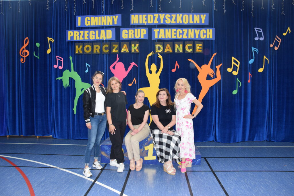 Pięć kobiet siedzące na podium na tle dekoracji z napisem I Gminny Międzyszkolny Przegląd Grup Tanecznych