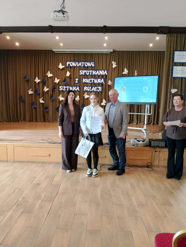 uczennica z dyplomem i nagrodą obok organizatorzy konkursu