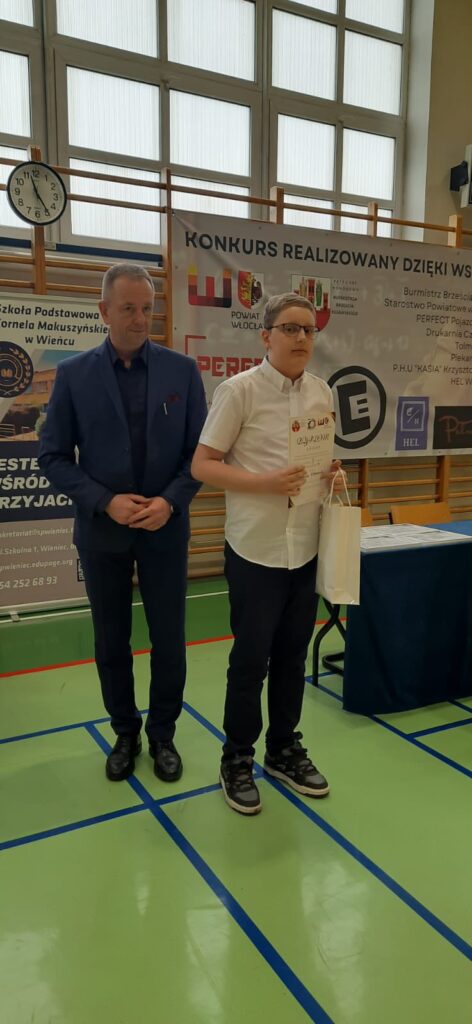 chłopiec w towarzystwie organizatorów z dyplomem i nagrodą