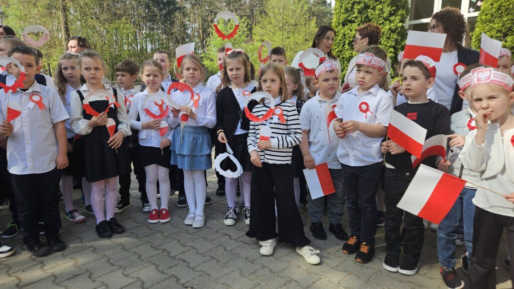uczniowie w strojach galowych z kotylionami i biało - czerwonymi flagami podczas apelu