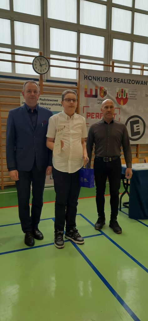 chłopiec w towarzystwie organizatorów z dyplomem i nagrodą