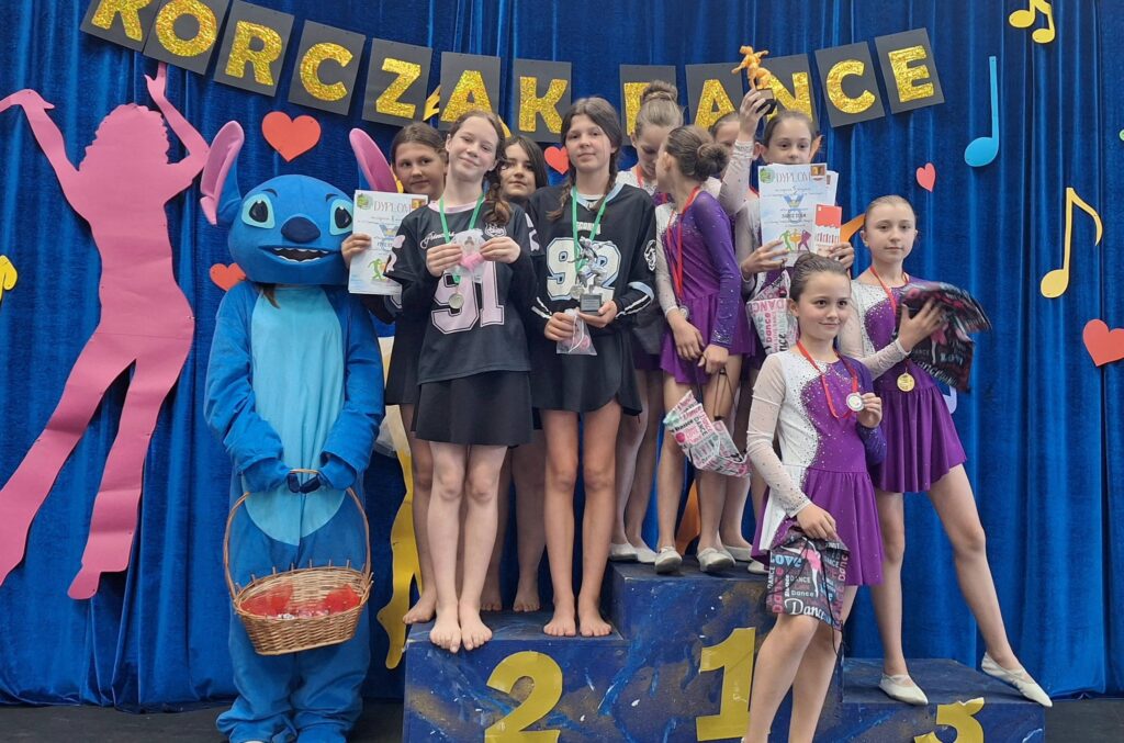uczestnicy przeglądu grup tanecznych w kolorowych strojach na podium
