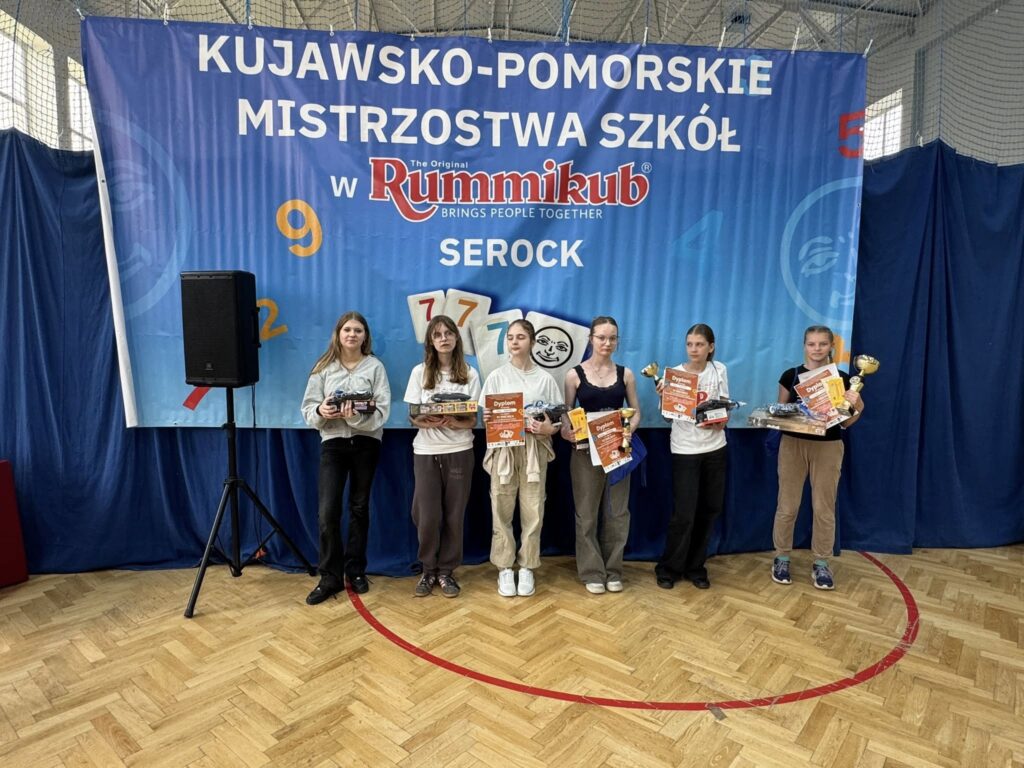uczniowie na tle plakatu kujawsko - pomorskie mistrzostwa szkół Rummikub z nagrodami