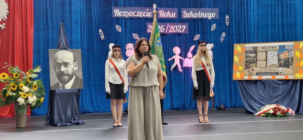 pani dyrektor, za nią uczniowie ze sztandarem szkoły na tle dekoracji na rozpoczęcie roku szkolnego