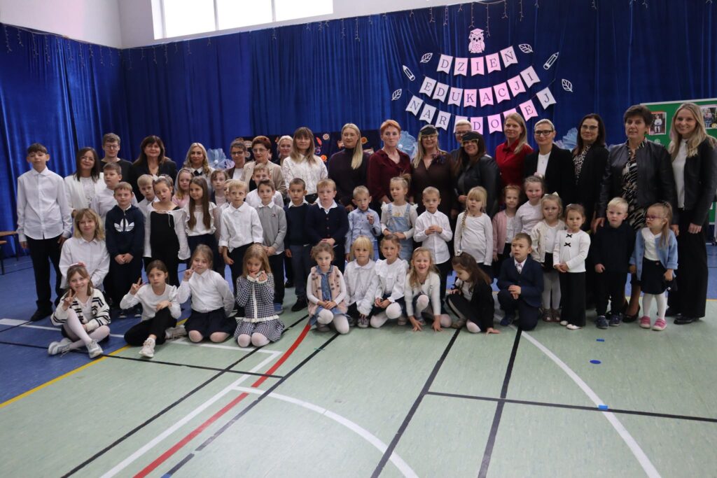 nauczyciele i uczniowie za nimi dekoracja z napisem dzień edukacji narodowej